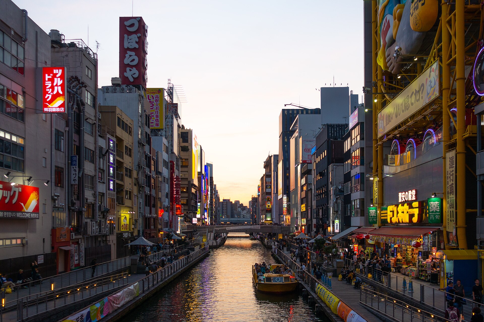 Canal de Dotonbori à Osaka au coucher du soleil, bordé d'enseignes lumineuses et d'un bateau.