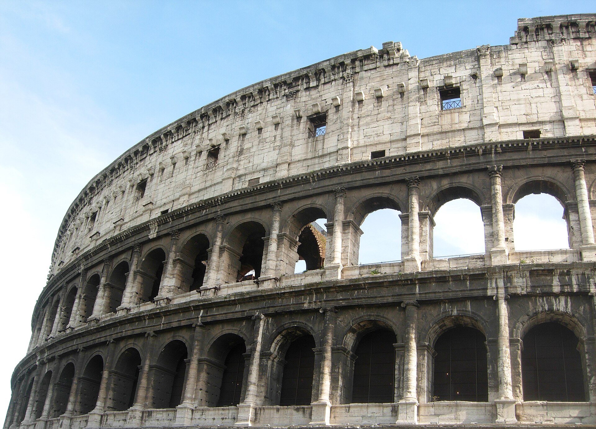 Vue extérieure du Colisée de Rome en journée, sous un ciel bleu.
