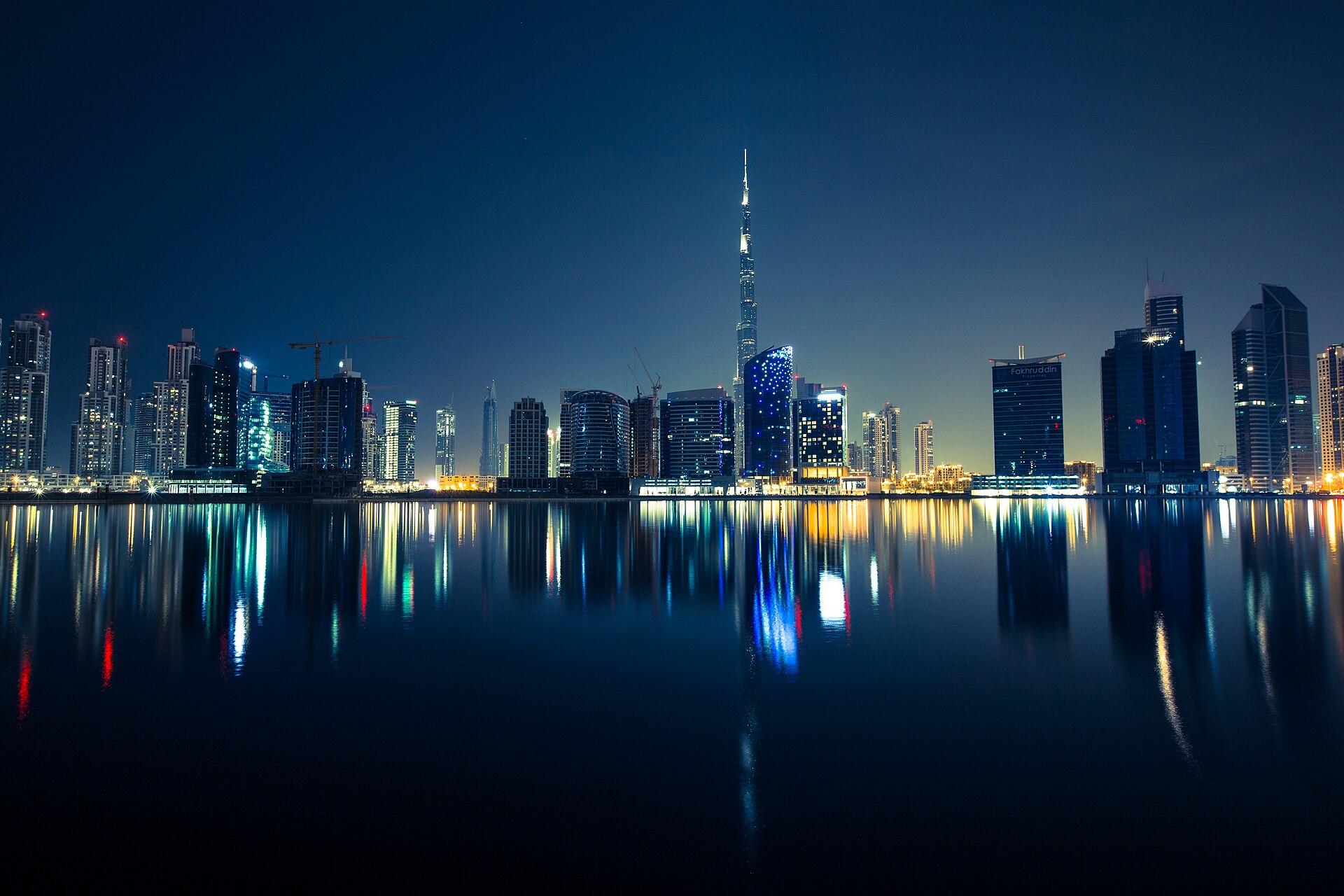 Vue nocturne du skyline de Dubaï avec la tour Burj Khalifa illuminée, reflétée dans l'eau.