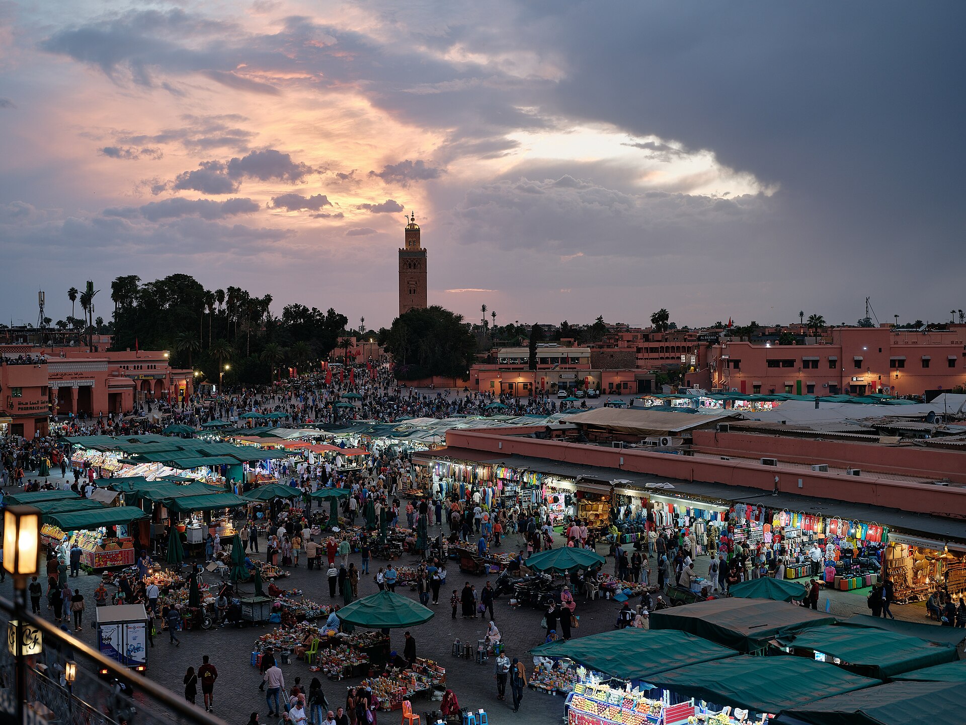 Vue en hauteur de la place Jemaa el-Fna à Marrakech animée, avec le minaret de la Koutoubia au coucher du soleil.