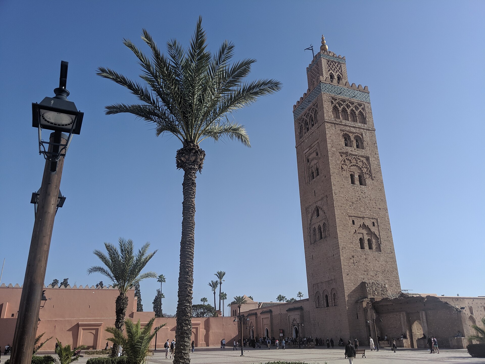 Minaret de la mosquée de la Koutoubia à Marrakech, avec un palmier au premier plan sous un ciel bleu.